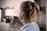 A woman drinks a cup of tea, wearing her hearing aid