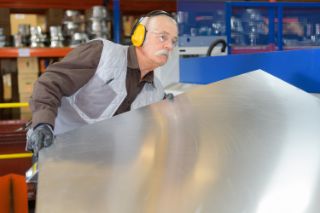 Senior man handling a metal sheet wearing earmuffs