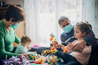 Grandparents wearing face masks playing with their grandchildren at home