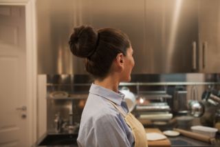 Una mujer de la tercera edad de perfil preparando comida en su cocina